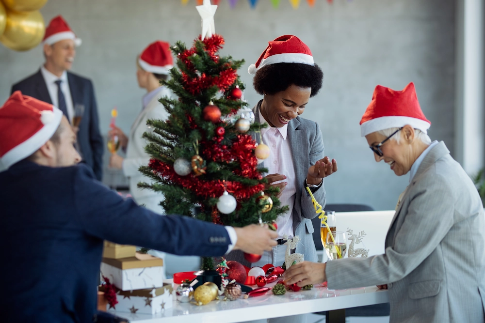 Happy colleagues decorating Christmas tree at a company christmas party in the office.